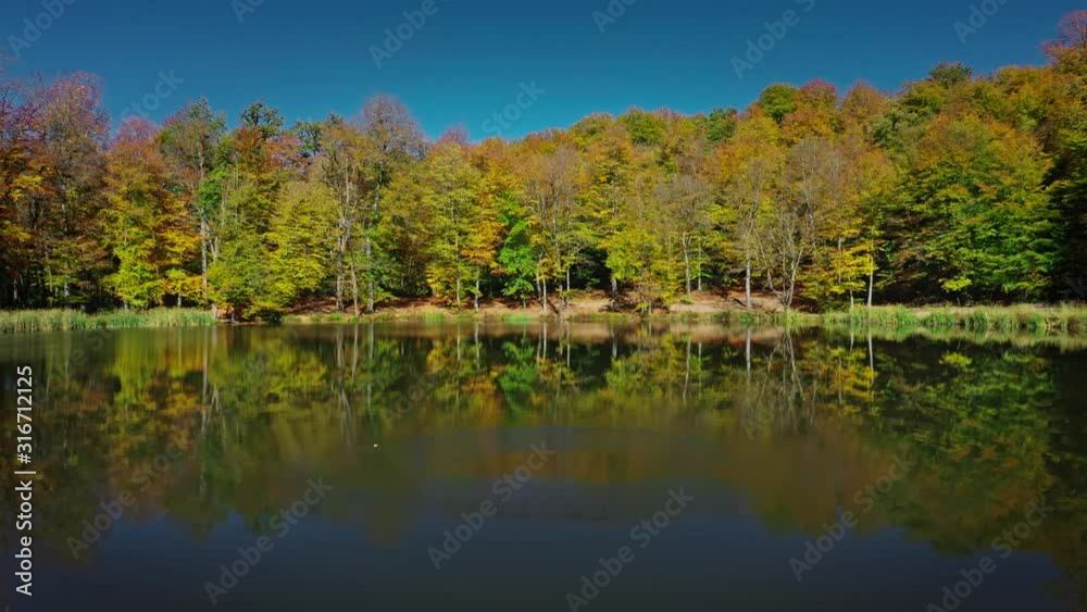Aerial drone zoom out of autumn forest trees near Gosh Lake in Armenia under bright blue sky. Colourful forest and water of Lake Sevan in armenian mountains in sunny day Aerial drone zoom out of autumn forest trees near Gosh Lake in Armenia under bright blue sky. Colourful forest and water of Lake Sevan in armenian mountains in sunny day