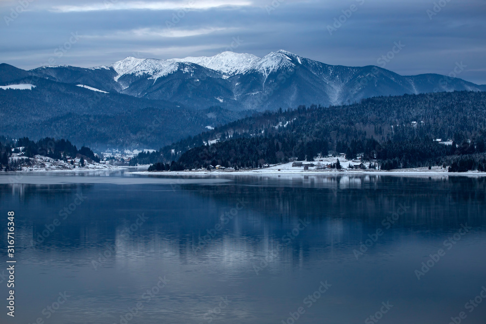 Frozen lake and pine trees in snow at Colibita. Romania early morning winter scen.