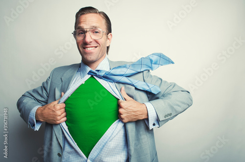Smiling businessman pulling open his suit to reveal an inner green superhero identity in the office