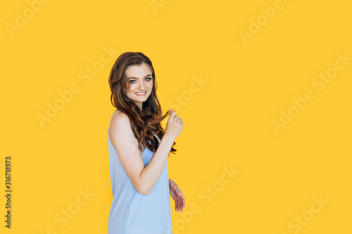 Portrait with copy space of young attractive smiling woman with holding hands on hair isolated on yellow background