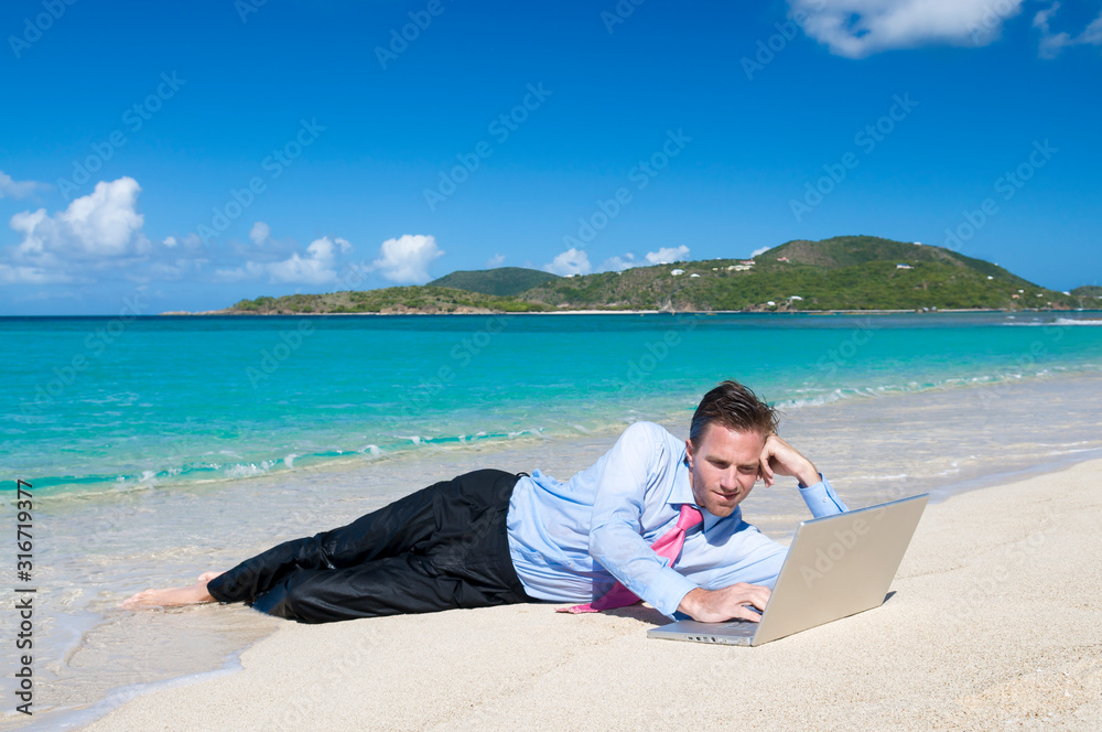 Relaxed businessman working on his laptop lying outdoors on the shore of a bright tropical beach
