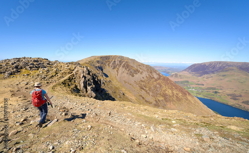 A female hiker walking off the summit of High Crag towards High Stile above Buttermere on a sunny day in the English Lake District.