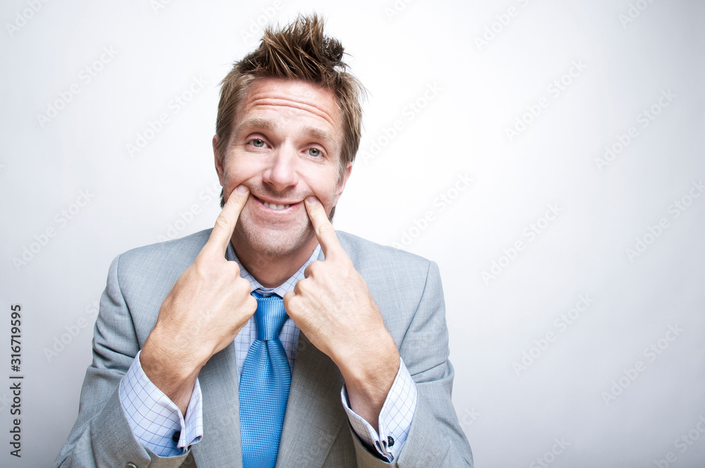 Tired businessman forcing a smile by holding up the corners of his mouth with his fingers Tired businessman forcing a smile by holding up the corners of his mouth with his fingers