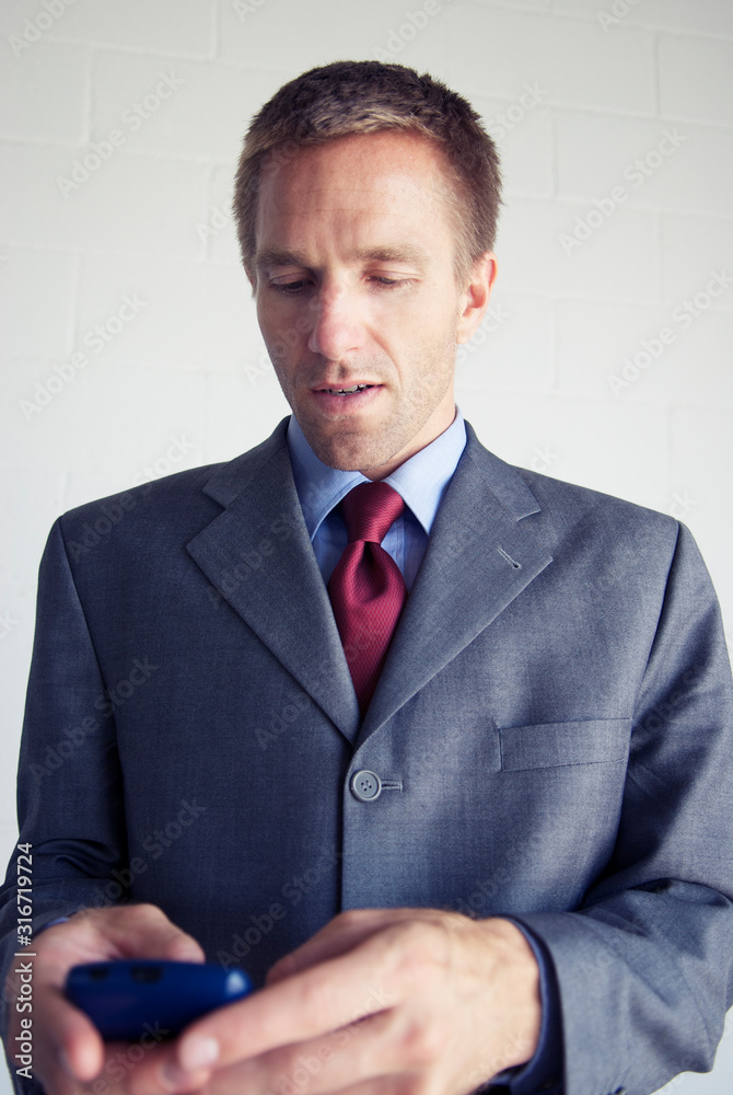 Distracted businessman standing looking down at his old-school pda smartphone device Distracted businessman standing looking down at his old-school pda smartphone device