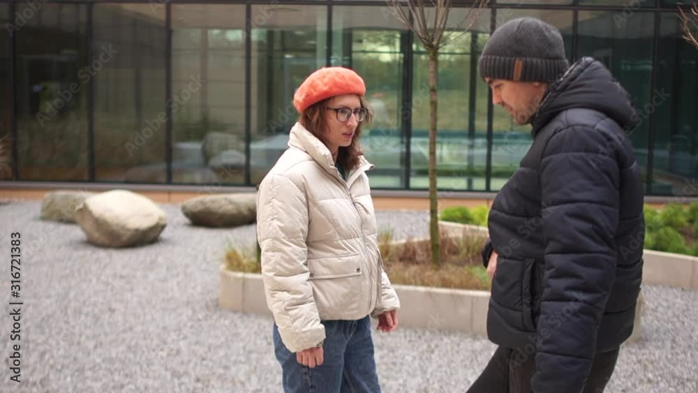 Woman in a white jacket helps secure while a young man in a black jacket and hat learns to walk again after a stroke or accident. Paralysis of extremities. Nearby is his girlfriend Woman in a white jacket helps secure while a young man in a black jacket and hat learns to walk again after a stroke or accident. Paralysis of extremities. Nearby is his girlfriend