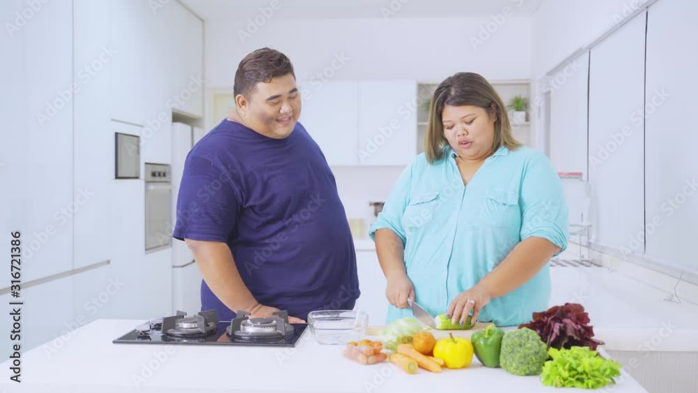 Young overweight couple making vegetable salad together in the kitchen at home. Shot in 4k resolution Young overweight couple making vegetable salad together in the kitchen at home. Shot in 4k resolution