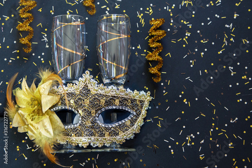 golden venetian mask with champagne glasses and confetti on black background
