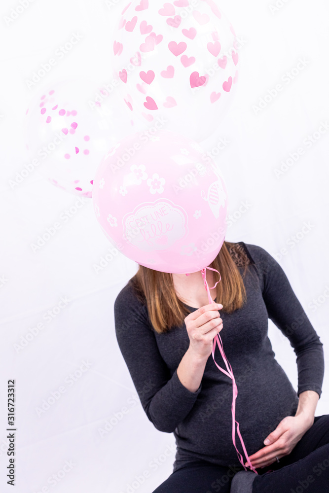 Fototapeta premium Young pregnant woman sitting with balloons - Gender Reveal - It's a Girl !