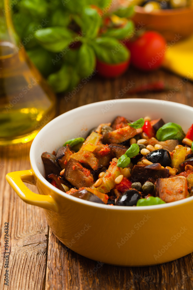 Traditional Italian caponata, served with croutons in a yellow, sunny pot. Decorated with basil and pine nuts. Traditional Italian caponata, served with croutons in a yellow, sunny pot. Decorated with basil and pine nuts.