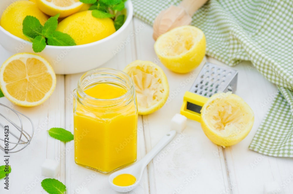 Homemade Lemon curd in glass jar with fresh lemons on a white wooden background. Horizontal orientation. Homemade Lemon curd in glass jar with fresh lemons on a white wooden background. Horizontal orientation.