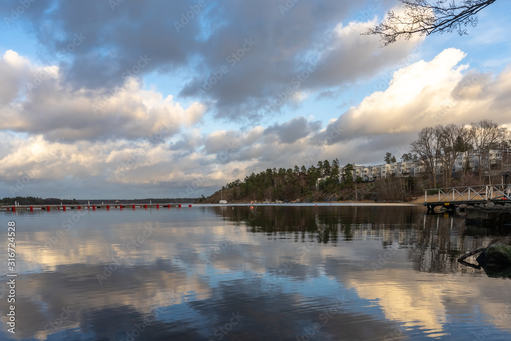 Panoramic view of Baltic Sea bay in spring. Landscape with beautiful clouds reflect on water. Horizon, skyline. Islands with pines and houses. Modern residence on the rocky shore. Archipelago, Sweden.