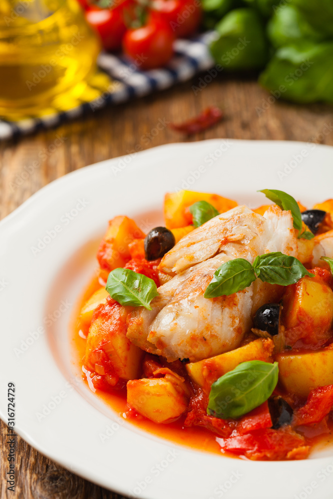 Traditionally prepared cod in Spanish. Served in tomato sauce with boiled potatoes, olivki and basil. Front view. Traditionally prepared cod in Spanish. Served in tomato sauce with boiled potatoes, olivki and basil. Front view.