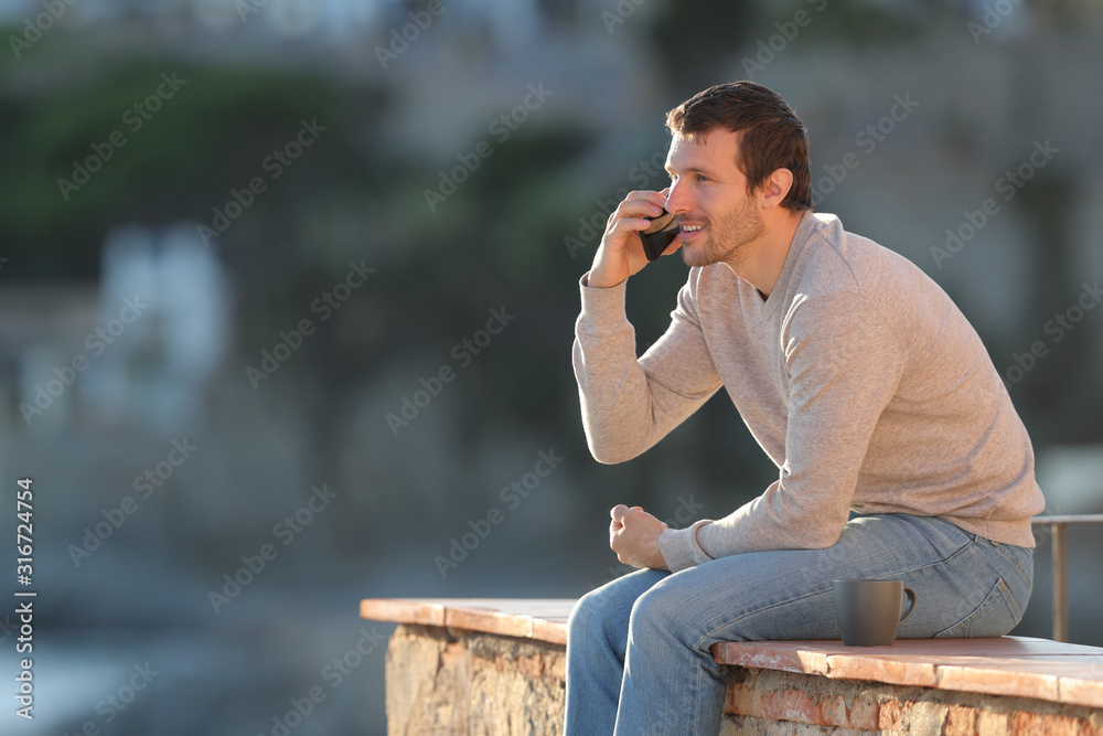 Fototapeta premium Happy man calls on mobile phone sitting on a wall