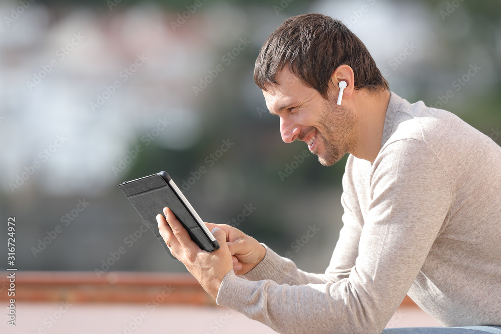 Obraz premium Profile of happy man watching media with tablet and earbuds