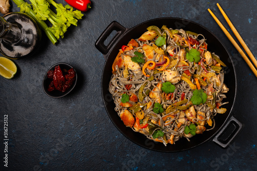 Wheat noodles with black sesame, fried in a wok with chicken and vegetables. Top view.