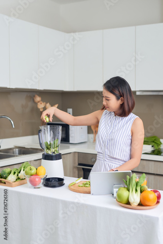 Beautiful Asian Woman juicing making green juice with juice machine in home kitchen. Healthy concept.