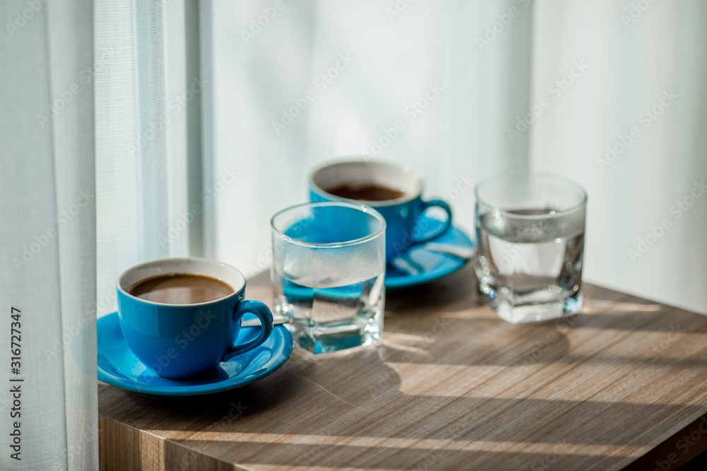 Obraz premium Close-up view of the blue coffee mug, clear glass for drinking water, placed on a tray to bring clear drinks, seen at resorts, hotels or bakeries