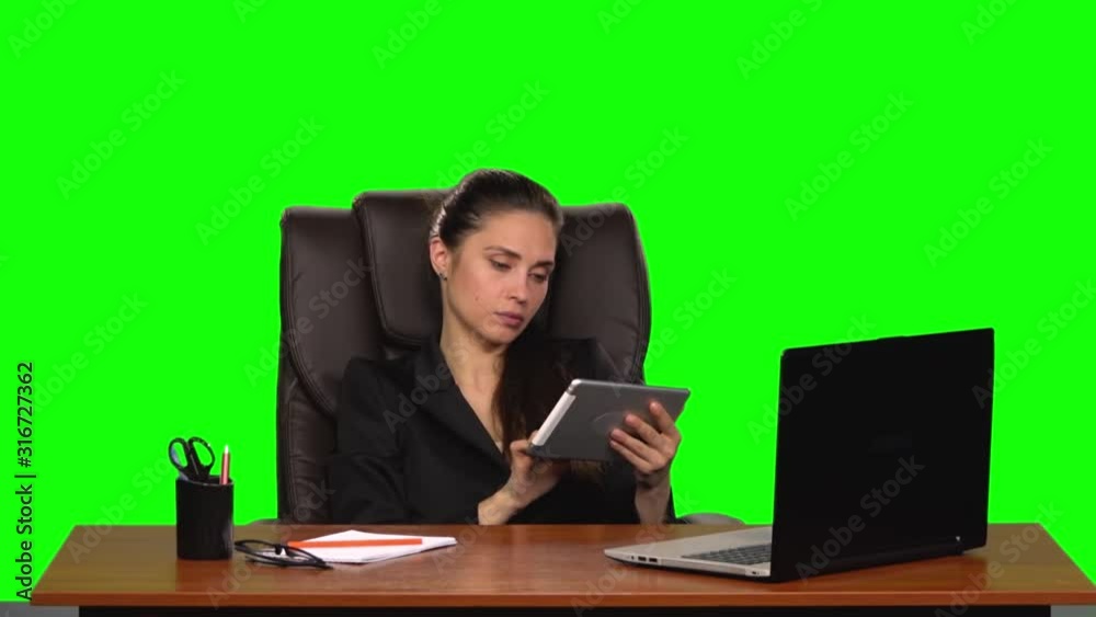 Worker girl sits at a workplace leaning back in a leather chair and communicates on a tablet and angry. Green screen. Slow motion Worker girl sits at a workplace leaning back in a leather chair and communicates on a tablet and angry. Green screen. Slow motion