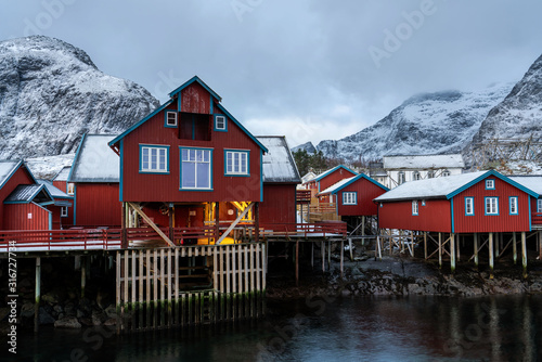 Red rorbu house of Lofoten village A with snowy mountains on horizon.