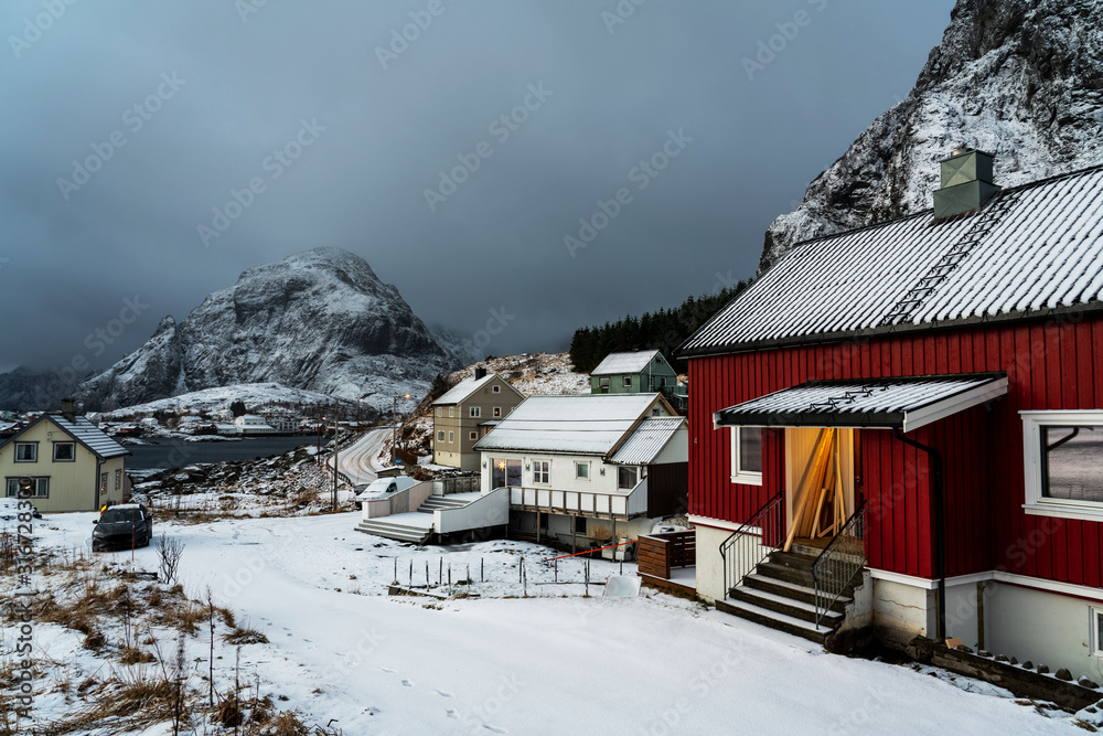 Lofoten Islands traditional village with red and white houses and snowy mountains on background.