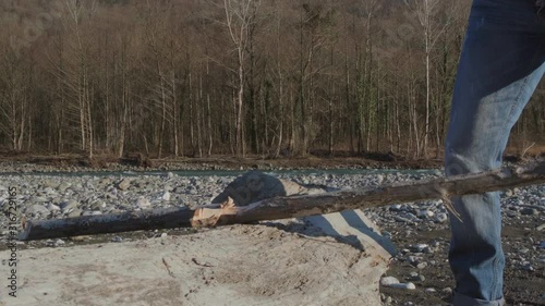 A man on a Sunny day on the Bank of a mountain river cuts a tree branch with an axe. A man prepares wood for a fire.
