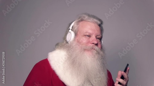 Senior Caucasian smiling man in Santa Claus suit with splendid grey hair, mustache and beard, dancing with sell phone and headgear. Funny portrait of handsome European people white background close up