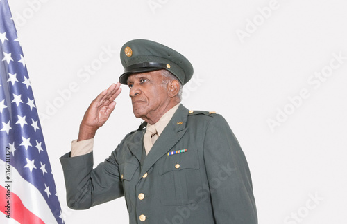 Senior male US military officer saluting American flag over gray background © moodboard