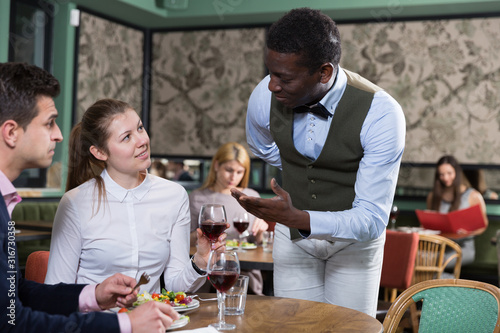 Positive couple talking with African American waiter