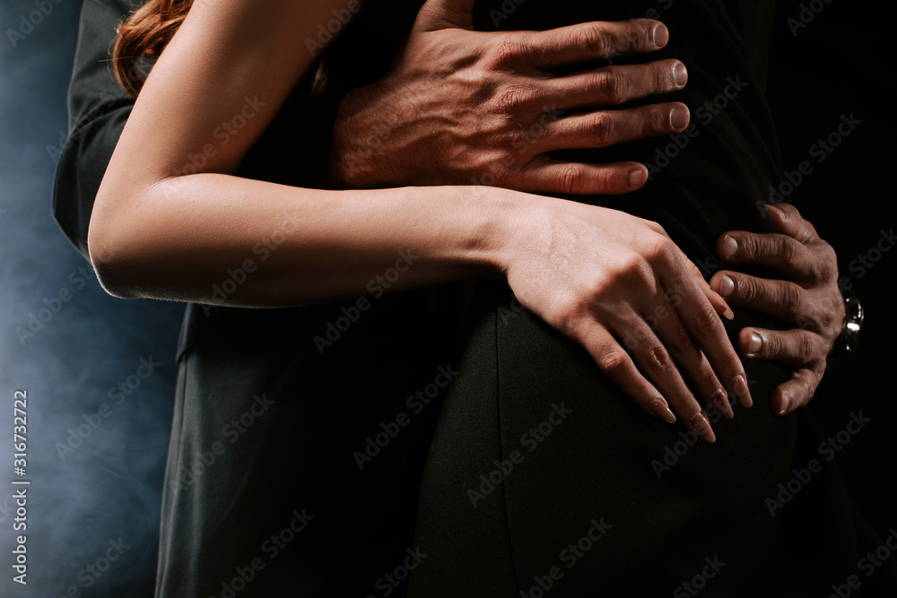 cropped view of man hugging woman on black with smoke cropped view of man hugging woman on black with smoke