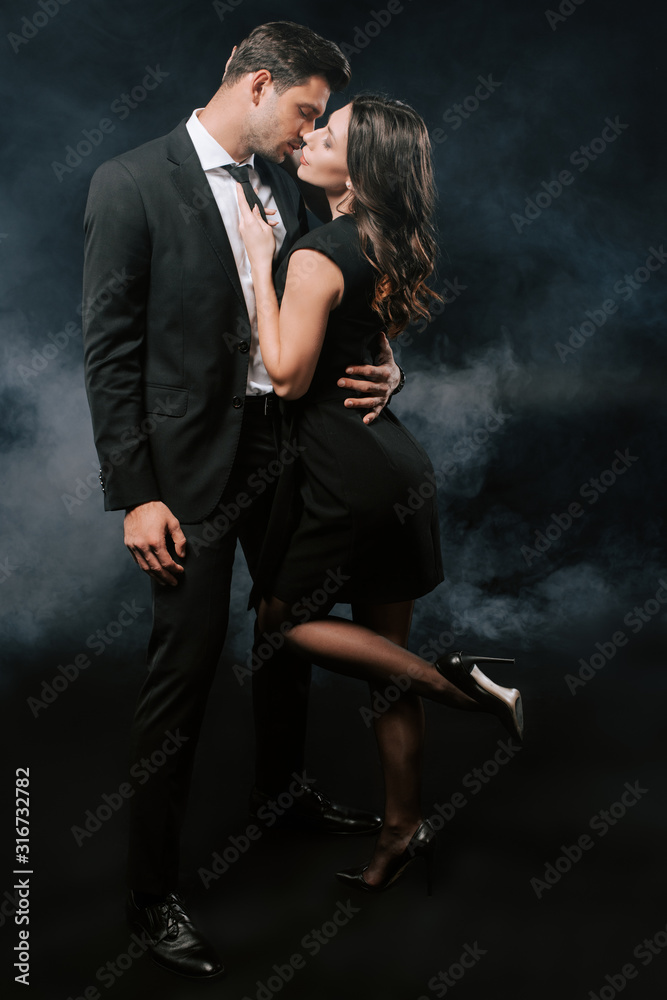 profile of handsome man in suit hugging woman in dress on black with ...