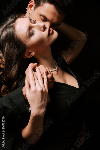 man embracing young woman in dress on black
