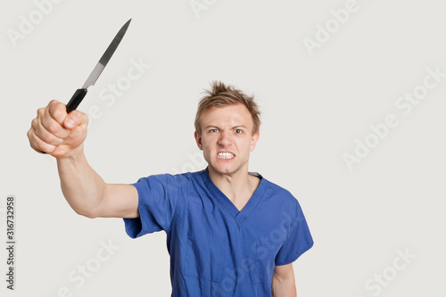 Angry male nurse threatening with knife over colored background