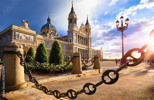 Madrid, Spain. Cathedral Santa Maria la Real de la Almudena at Plaza de la Armeria. Famous landmark with sunset sun rays. Street lamps and picturesque sky with clouds. photo