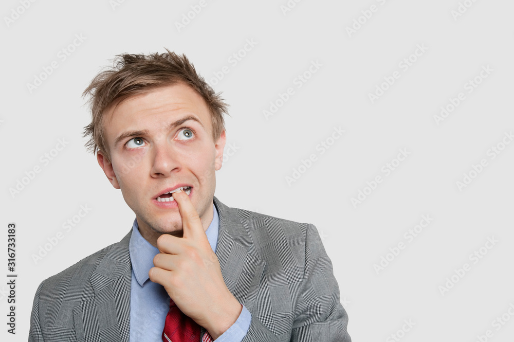 Thoughtful young businessman biting finger while looking up over colored background Thoughtful young businessman biting finger while looking up over colored background