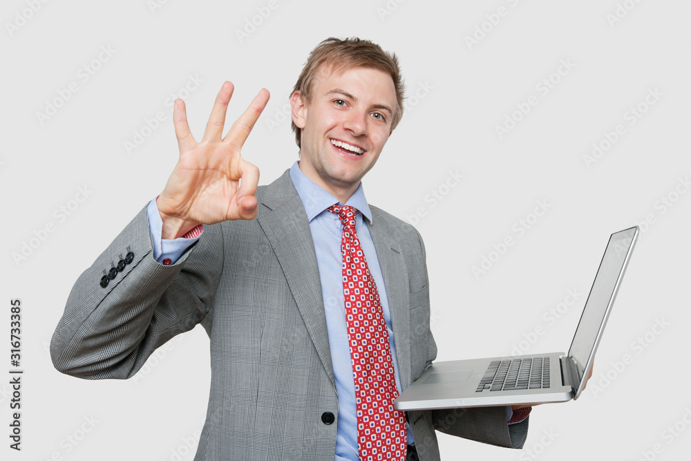 Portrait of cheerful businessman with laptop gesturing ok sign over colored background Portrait of cheerful businessman with laptop gesturing ok sign over colored background
