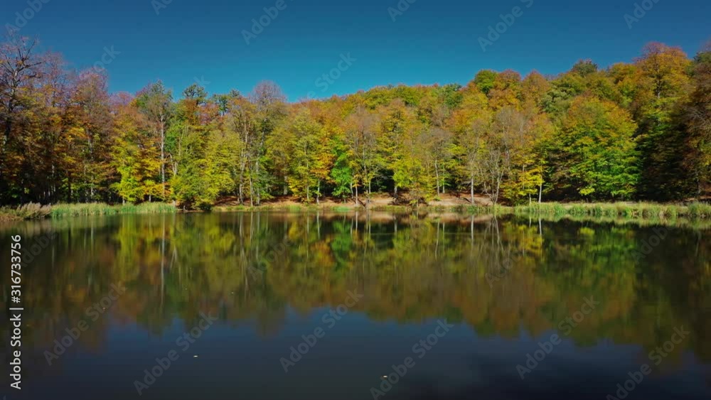 Aerial drone pan shot right to left of autumn forest trees nearGosh Lake in Armenia under bright blue sky. Colourful forest and water of Gosh Lake in armenian mountains in sunny day Aerial drone pan shot right to left of autumn forest trees nearGosh Lake in Armenia under bright blue sky. Colourful forest and water of Gosh Lake in armenian mountains in sunny day
