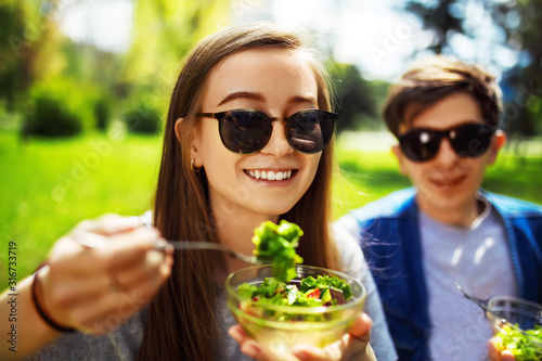 Young couple enjoying lunch outdoor on sunny day. Happy young friends eating natural vegetable salad for lunch. Healthy lifestyle. Concept picnic. Clean eating, vegan food concept.