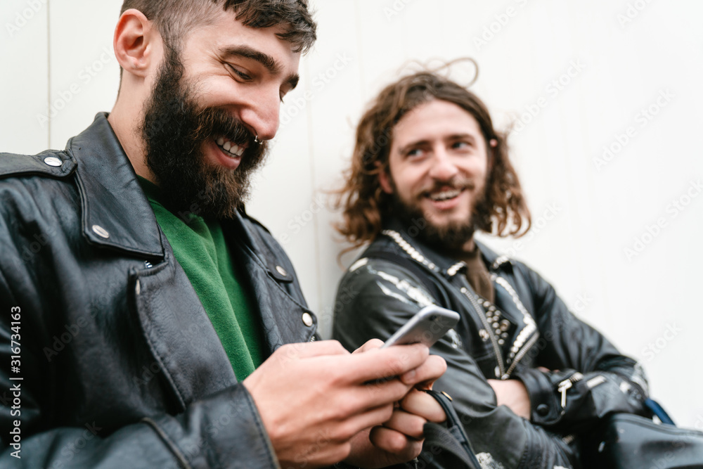 Fototapeta premium Photo of bearded joyful men bikers using cellphone and smiling