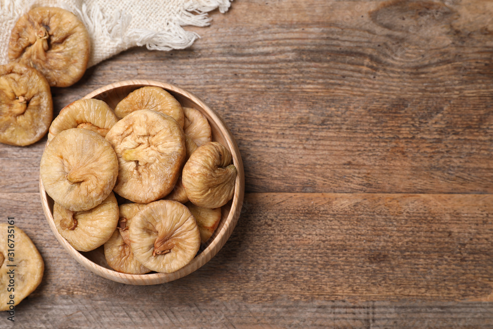 Tasty dried figs in bowl on wooden table, top view. Space for text