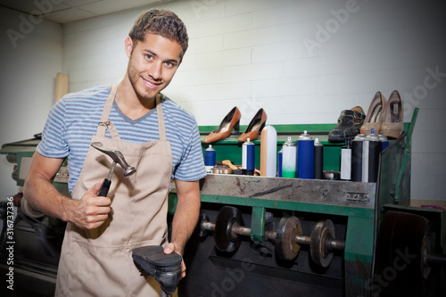 Fototapeta Young shoemaker hammering shoe sole in workshop
