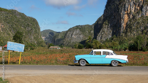 baby-blue cuban classic car in the vinales landscape with a street sign, meadows and mountains, cuba