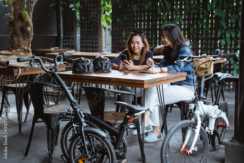 two young woman relaxing discuss and using cell phone when a break at cafe after cycling