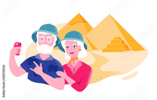 Senior couple in safari hats is taking selfie near the Egyptian pyramids. Active leisure for older people.