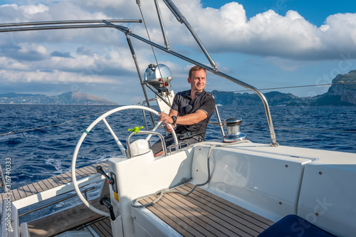Sailor at the helm of modern sailing yacht. Mediterranean sea, near Ischia island and Capri island on the background, Italy.