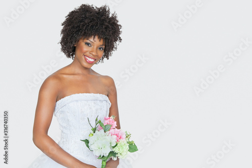 Portrait of beautiful African American bride holding bouquet over gray background