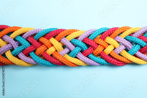 Braided colorful ropes on light blue background, top view. Unity concept