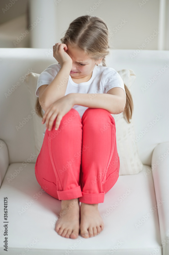 Little girl crying while sitting on sofa Stock Adobe Stock