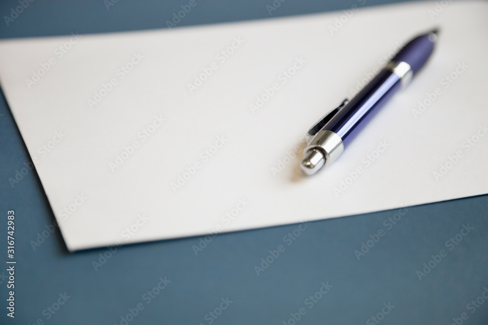 Metallic pen on a blank white paper over dark blue background Metallic pen on a blank white paper over dark blue background
