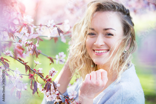 Young woman enjoying the nature in spring. Breathing fresh air and flowers aroma in beautiful park with cherry trees in bloom. Happiness concept