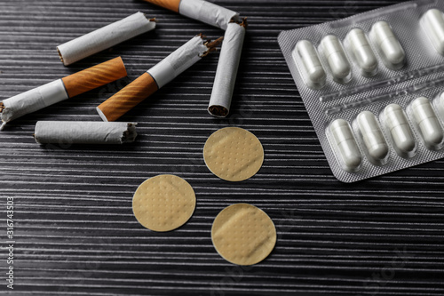 Obraz na plátne Nicotine patches, pills and broken cigarettes on black table, above view